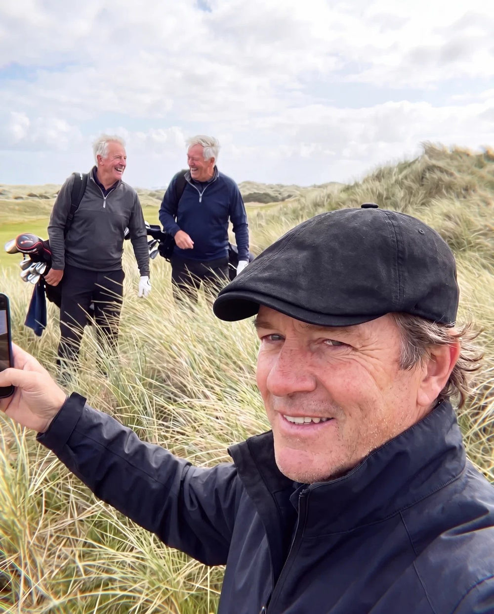 Golfer selfie on a windy links course with his two playing partners, black flat cap