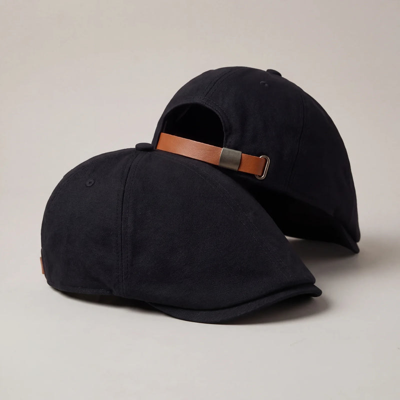 Two black no-logo flat caps, the pair, with brown leather back strap